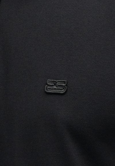 Μαύρο υφασμάτινο ύφασμα με μικρό, ανάγλυφο κεντημένο λογότυπο "25" σε ταιριαστό μαύρο νήμα, στο κέντρο της επιφάνειας.