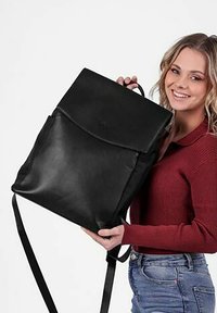 Černý kožený batoh s klopou, vybavený nastavitelnými popruhy a přední kapsou. Hladký povrch, jednoduchý design a žádné viditelné kovové prvky.