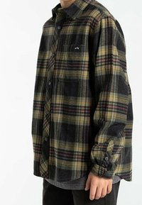 Camicia di flanella a quadri neri, verdi e gialli, con design a bottoni, maniche lunghe e una tasca sul petto con etichetta.