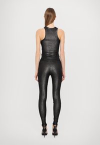 Top nero fitted senza maniche e leggings realizzati in un materiale lucido e texturizzato. L'outfit è abbinato a scarpe con tacco alto nere.