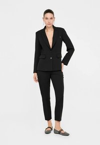 Zwart op maat gemaakt pak met een colbert met inkeping, voorzien van twee voorzakken en een enkele knoopsluiting, gecombineerd met slim-fit broek.