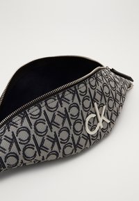 Borsetta con zip con motivo monogramma bianco e nero di Calvin Klein e logo CK argento sul davanti, parzialmente aperta che mostra l'interno scuro.