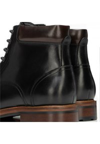 Černé kožené kotníkové boty s hladkou texturou, hnědými koženými doplňky na límci a dřevěným podpatkem s dvěma černými pruhy.