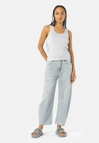 Canotta grigia a coste, jeans a gamba larga lavaggio chiaro con dettagli strappati, e pantofole pelose grigie. Outfit semplice e casual.