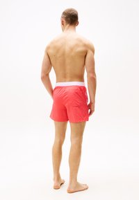 Pantaloni scurți de înot pentru bărbați, în coral strălucitor, cu un brâu elastic alb. Caracteristici includ un buzunar la spate și un material ușor, ce se usucă rapid.