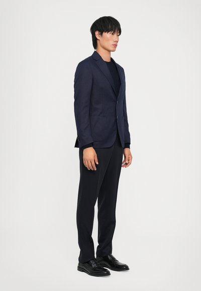 Navy blue tailored blazer with two buttons, notch lapels, and side pockets, paired with matching trousers and black leather shoes.