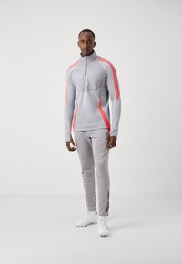 Lichtgrijze sportieve trainingspak met roze accenten, bestaande uit een ritsjack met hoge kraag en tapered broek met zijstrepen en gestructureerde details.