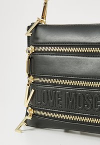 Black leather handbag featuring multiple gold-tone zippers, embossed "LOVE MOSCHINO" detail, and distinctive gold hardware accents.