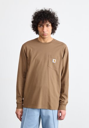 Long-sleeve brown cotton shirt with a chest pocket featuring a small logo. Model wears light blue straight-leg pants. Simple design, relaxed fit.