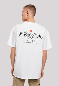 White cotton t-shirt with a mountain graphic, black outlines, a red sun, and text "ESCAPE AND DISCOVER THE WORLD" on the back.