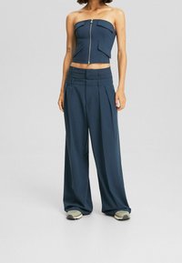 Mörkblå strapless topp med central dragkedja och två framfickor, i kombination med vida navybyxor med veck och en strukturerad midja.