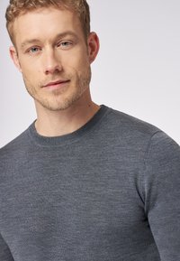 Grau gestrickter Rundhalspullover aus weichem Stoff, mit schmaler Passform und gerippten Bündchen. Die Textur ist glatt mit einem leichten Glanz.