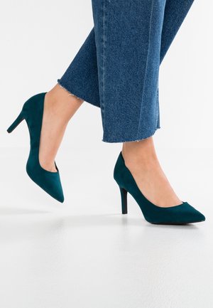 Blågrønne ruskind høje hæle med spids tå og en 10 cm stiletthæle; blød tekstur og rene linjer; kombineret med brede denim culotter.