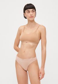 Beige bikiniset bestående av en crop top med tynne stropper og matchende lave briefs. Myk, glatt stoff med en delikat sløyfedetalj på briefs.