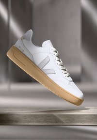 Witte leren sneaker met een tan kleurige rubberen zool, getextureerde accenten en vetersluiting. Beschikt over een geperforeerd ontwerp en een merkembleem op de zijkant.