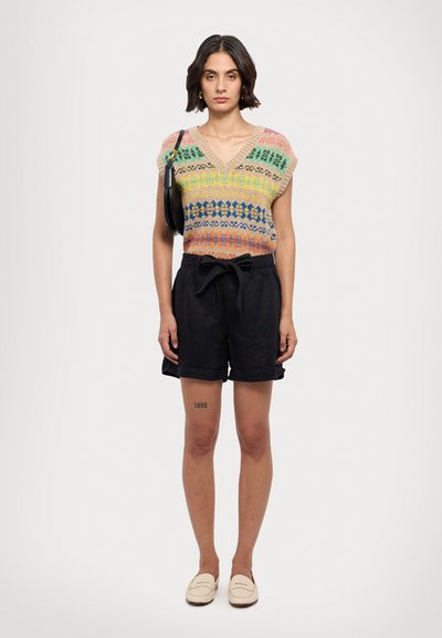 Pulover tricotat multicolor cu decolteu în V și modele, asortat cu pantaloni scurți negri cu talie înaltă. Modelul poartă loafers crem și ține o geantă neagră.