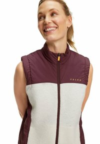 Ärmellose Weste mit einem burgunderfarbenen Oberteil und einem cremefarbenen Fleece-Frontpanel, ausgestattet mit einem hohen Kragen und dem goldenen "FALKE"-Logo auf der Brust.