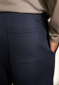 Pantaloni blu navy in tessuto a coste, con tasca cucita sul retro e vita elastica. Finitura uniforme e dalla texture liscia.