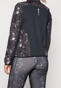 Černá a šedá sportovní bunda s mramorovaným vzorem, texturovaná látka a vysoký límec. Obsahuje jemné logo na zadní straně a kontrastní švy.