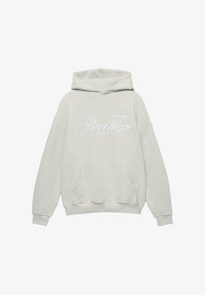 Felpa con cappuccio grigia chiara con tasca frontale, caratterizzata da testo ricamato bianco: "Galleria d'Arte Brooklyn Fondata nel 1991." Texture del tessuto morbida.