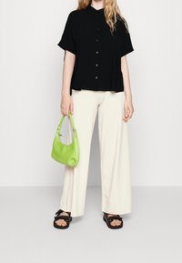 Svart kortärmad skjorta med knappar, krämfärgade vida byxor och en liten grön handväska. Svarta sandaler med dubbelbandsdetalj.