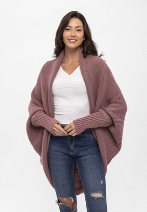 Knitted cardigan in soft mauve, featuring a wide shawl collar, ribbed sleeves, and a relaxed fit. Paired with distressed blue jeans.