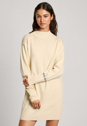 Abito in maglia color crema con colletto alto, polsini a coste e dettagli con logo sulla manica, caratterizzato da una vestibilità ampia e rilassata.