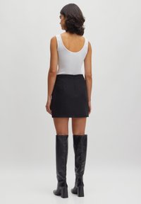 Witte tanktop, zwarte minirok en kniehoge zwarte leren laarzen. De outfit heeft een zachte textuur en een getailleerde silhouet.