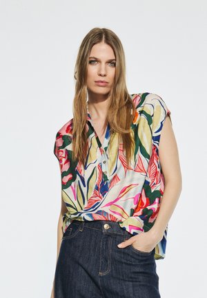 Short-sleeve shirt in light fabric with colorful floral print, V-neck, and button detail. Paired with dark jeans.