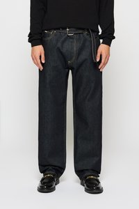 Dark blue denim jeans with a relaxed fit, featuring yellow stitching and a standard zipper fly. Paired with black shoes.