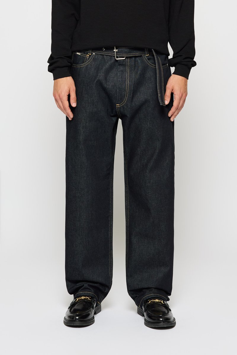 Dark blue denim jeans with a relaxed fit, featuring yellow stitching and a standard zipper fly. Paired with black shoes.