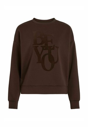 Sweatshirt marron avec un design court, présentant "SOIS TOI" en grandes lettres texturées d'une teinte marron plus foncée. Tissu doux et manches longues.