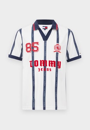 Valge polo särk, millel on tumesinised vertikaalsed triibud, tumesinine krae ja varrukad, punane "85" ja "Tommy Jeans" tekst ning punane vapp emblüüm rinnal.