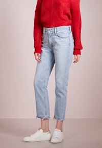 Ljusblå jeans med rak passform och fransad fåll, i kombination med vita sneakers och en röd strukturerad stickad tröja.