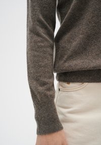 Brun ylletröja med ribbad manschett, kombinerad med ljusa jeans. Texturen verkar mjuk, med ett subtilt mönster i tyget.