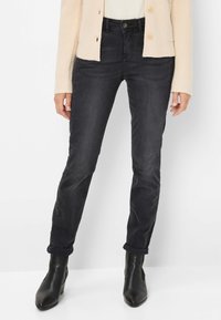 Jeans in denim nero con una vestibilità slim e una leggera elasticità. Abbinamento con un cardigan leggero a maglia. Cuffie arrotolate e stivaletti neri alla caviglia completano il look.