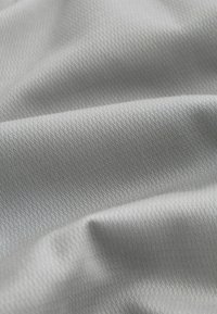 Helles graues Gewebe mit einer strukturierten Oberfläche, das ein dezentes geometrisches Muster aufweist. Das Material wirkt glatt und flexibel und fällt weich.