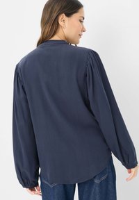 Marinebluse med lange, puffede ærmer og løs pasform. Har en klassisk krave og glat tekstur, båret med blå jeans.