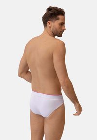 Witte boxershorts met een roze tailleband, vervaardigd uit een gladde stof en met een strakke pasvorm, van achteren getoond op een model met kort haar.