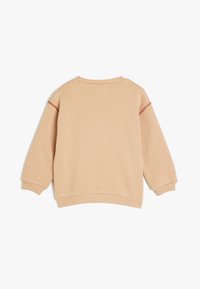 Vaalean beige collegepaita, jossa on pyöreä pääntie, ribbed hihansuut ja helma, sekä punaiset ompeluakoristukset hartioilla. Pehmeä, teksturoitu kangas.
