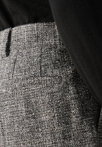 Grå tweedbyxor med ett texturerat mönster, med flat front och sidofickor, i kombination med en svart topp.