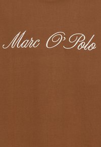 Tela marrón con texto bordado en cursiva blanca "Marc O’ Polo" centrado en la superficie.