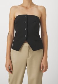 Top nero senza spalline con sei bottoni sulla parte anteriore, design strutturato e vestibilità sartoriale. Abbinato a pantaloni beige a vita alta.