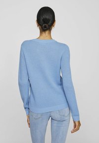 Helles blaues Strickoberteil mit einem strukturierten Muster, Rundhalsausschnitt und gerippten Bündchen und Saum. Trägt einen hellblauen Jeans.