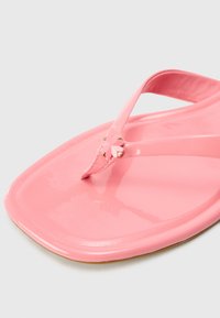 Infradito rosa lucido con un motivo a forma di cuore sulla cinghia, con suola piatta e superficie liscia.