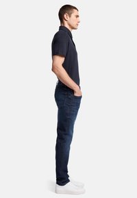 Polo shirt blu navy abbinato a jeans blu scuro e sneakers bianche. La camicia ha un colletto e maniche corte, con una silhouette aderente.