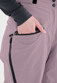 Vaalean violetit lasketteluhousut, joissa on vetoketjullinen tasku, sileä pinta ja muotoiltu muotoilu, mustilla varusteilla.