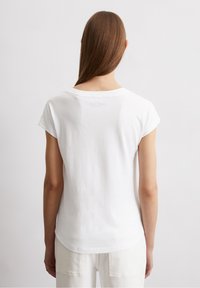 Vit bomull t-shirt med avslappnad passform, korta ärmar och rundad halsringning. Har en diskret logotryck på den övre ryggen.