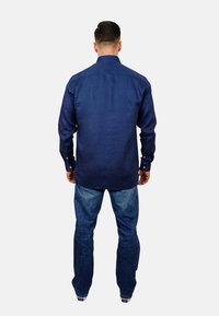 Mörkblå linneskjorta med rak fåll, knappade ärmar och krage, tillsammans med ljusblå jeans och svarta sneakers.