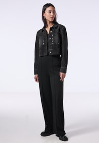 Mustat lyhyet farkkutakit, joissa on hopeiset niitit, isot etutaskut ja napsautettavat napit, yhdistettyinä korkeavyötäröisiin mustiin housuihin ja paksupohjaisiin saappaisiin.